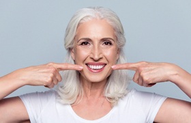 senior woman with all on four dental implants pointing to her smile