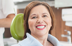 Smiling woman with dental crown supported fixed bridge restoration in dental chair