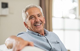 Older man with dental implants in DeLand smiling on couch