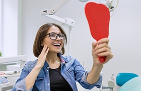 Woman holding mirror and smiling at her dental implants in DeLand