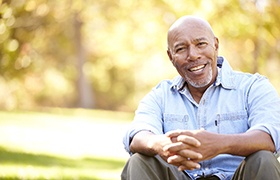 Older man with dental implants in DeLand smiling with folded hands