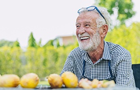 older man smiling outside with lemons on table