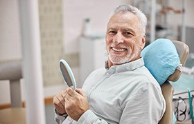 man smiling while holding dental mirror