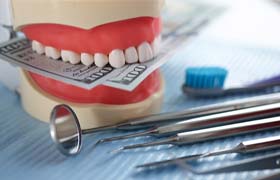 artificial teeth holding money with dental tools