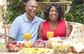 couple sitting at a table outside with various foods and beverages