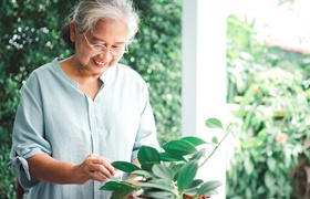 A person with dental implant supported dentures tending to their houseplants and smiling