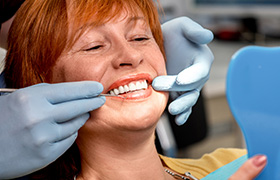 Senior woman looking at smile in mirror after dental implant tooth replacement