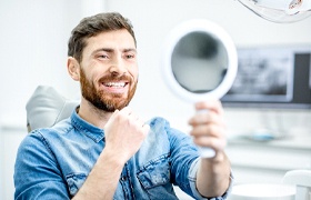 man smiling in mirror after smile makeover in DeLand